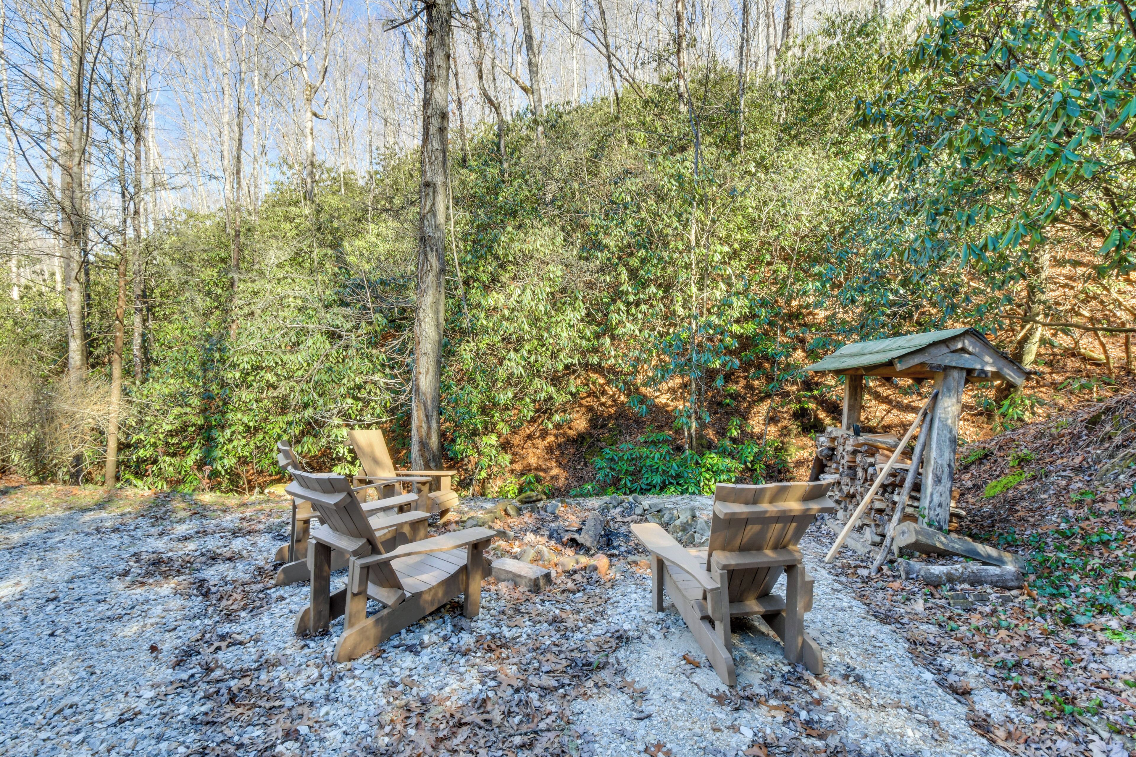 Un área de estar al aire libre de estilo rústico con sillas de madera y una pequeña estructura de madera, rodeada de un bosque denso.