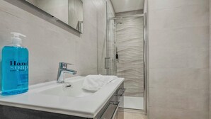 Une salle de bain moderne avec un lavabo blanc, un flacon de savon liquide et une cabine de douche en verre.
