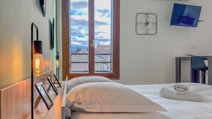 Une chambre d’hôtel avec un lit, une table de chevet avec une lampe, une horloge et un téléviseur fixé au mur.