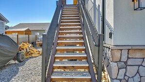 Un escalier en bois mène à un espace abrité, doté d’un mur en pierre et d’une rambarde en métal.