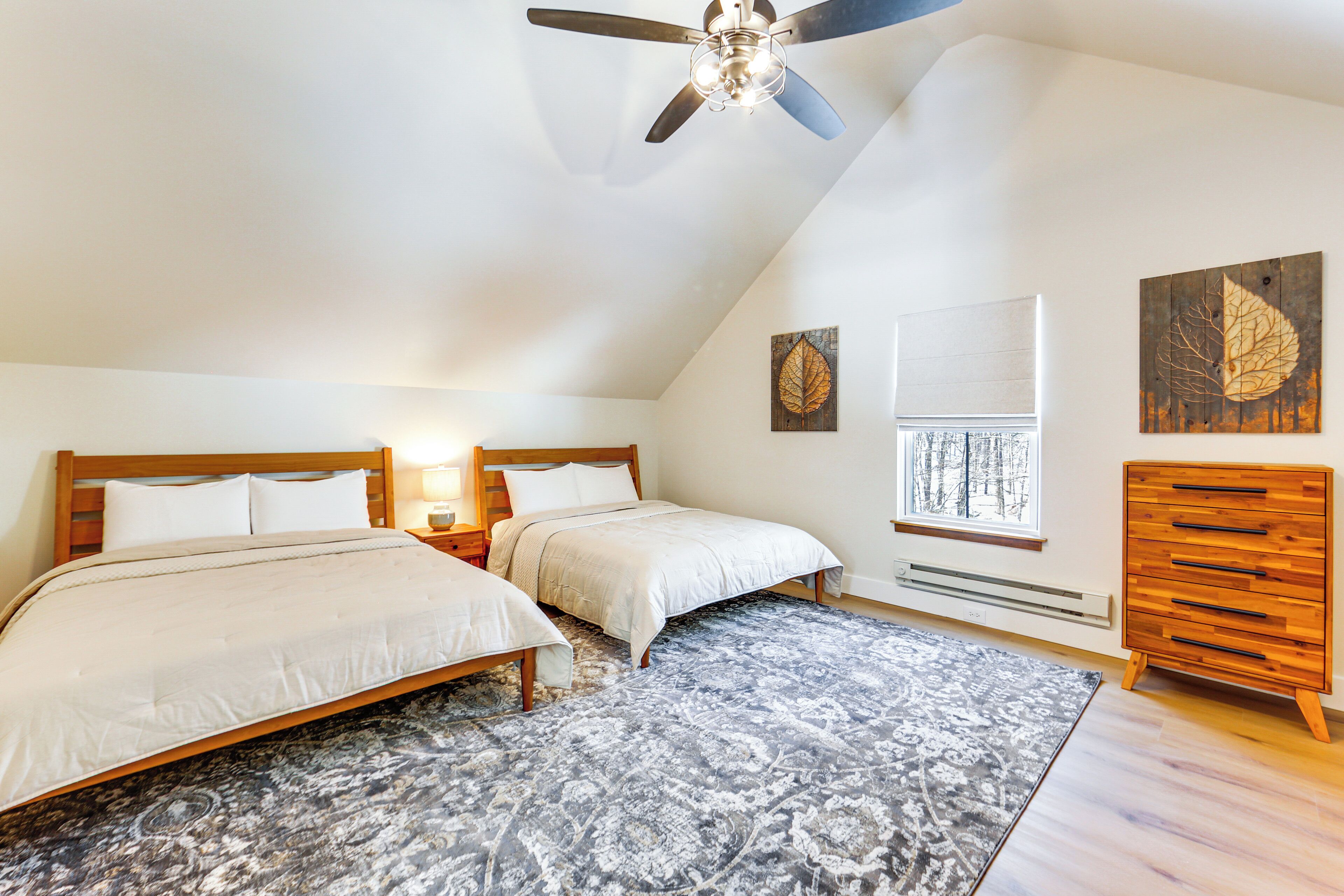 A bedroom with two beds, a ceiling fan, a window with a view, and a wooden dresser.