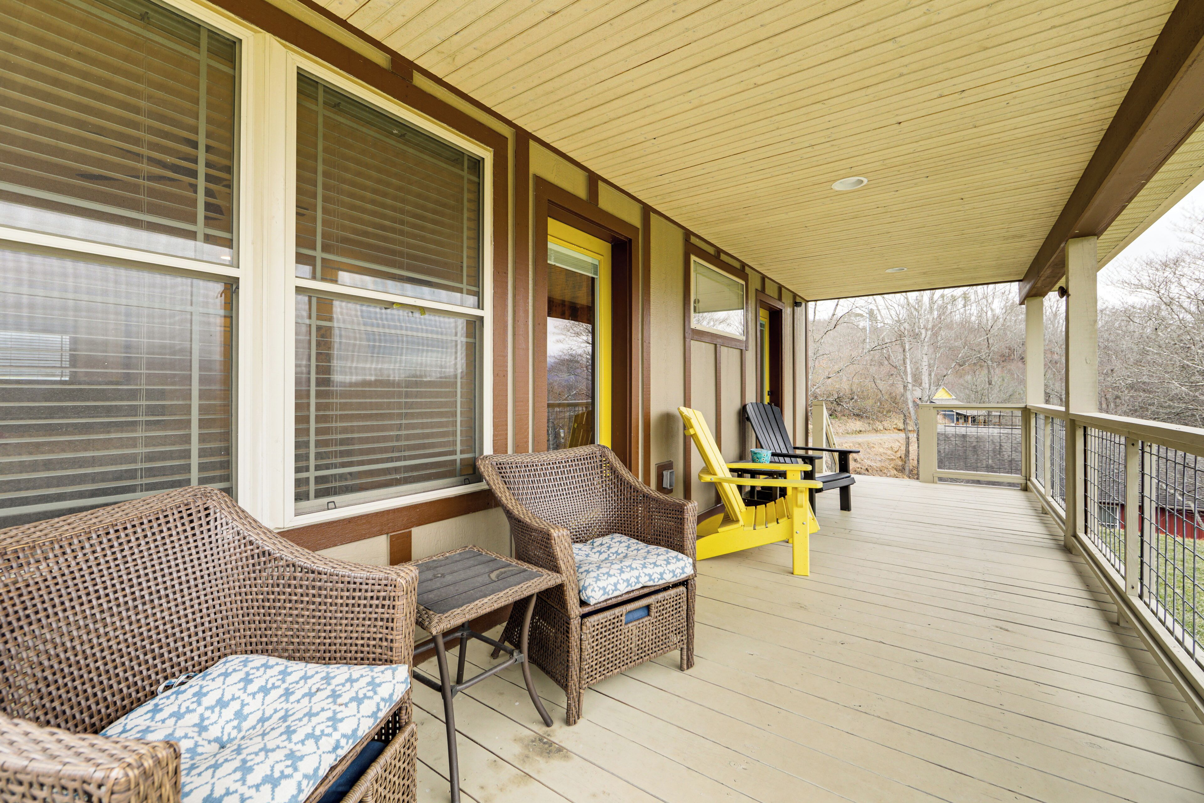 A covered porch with wicker furniture and a yellow Adirondack chair.