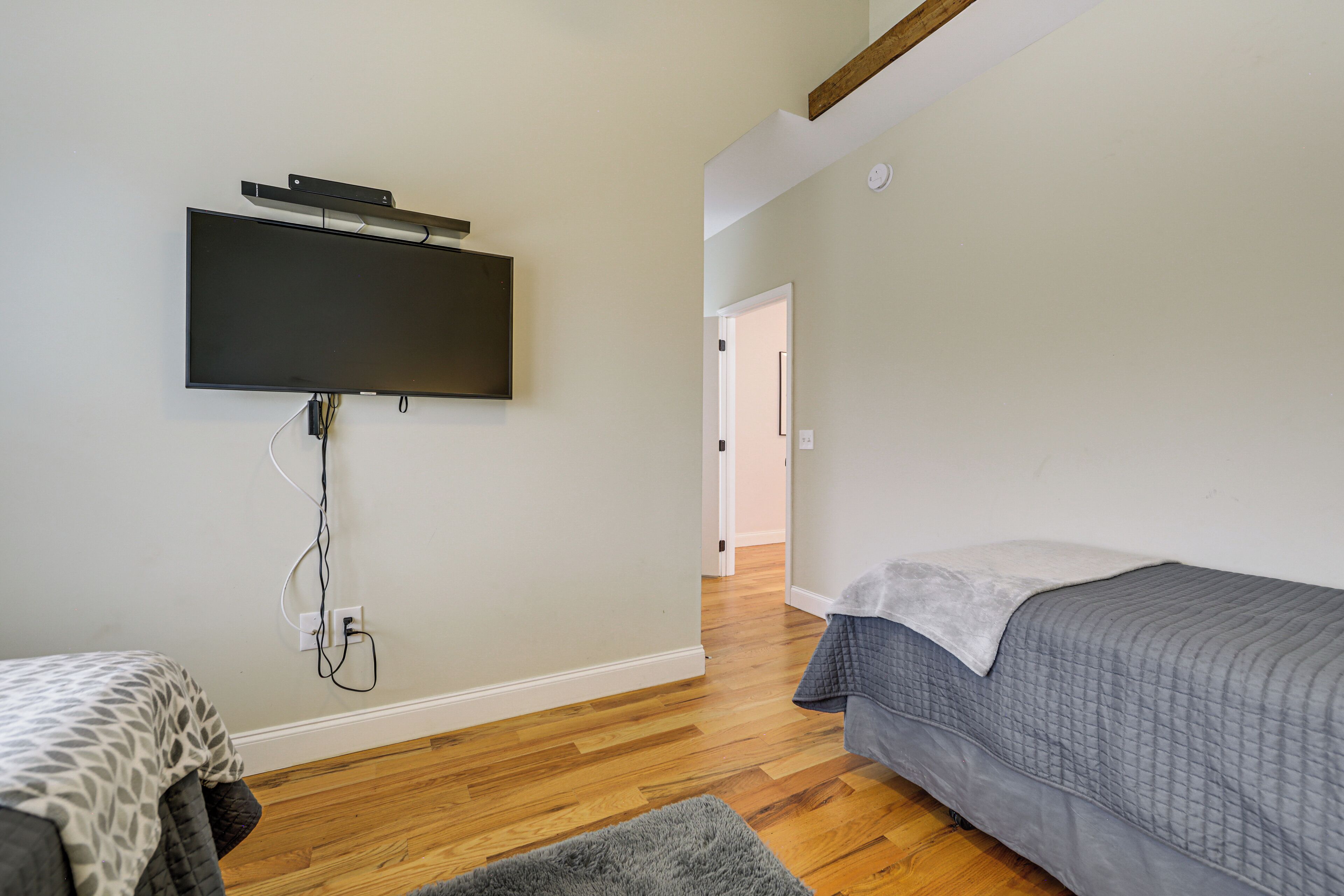 Quarto com cama, televisão fixada na parede e piso de madeira.