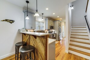 A modern kitchen with a central island, bar stools, and a staircase leading to another level. - Hot Tub + Blue Ridge Mtn Views: Waynesville Home (Waynesville)