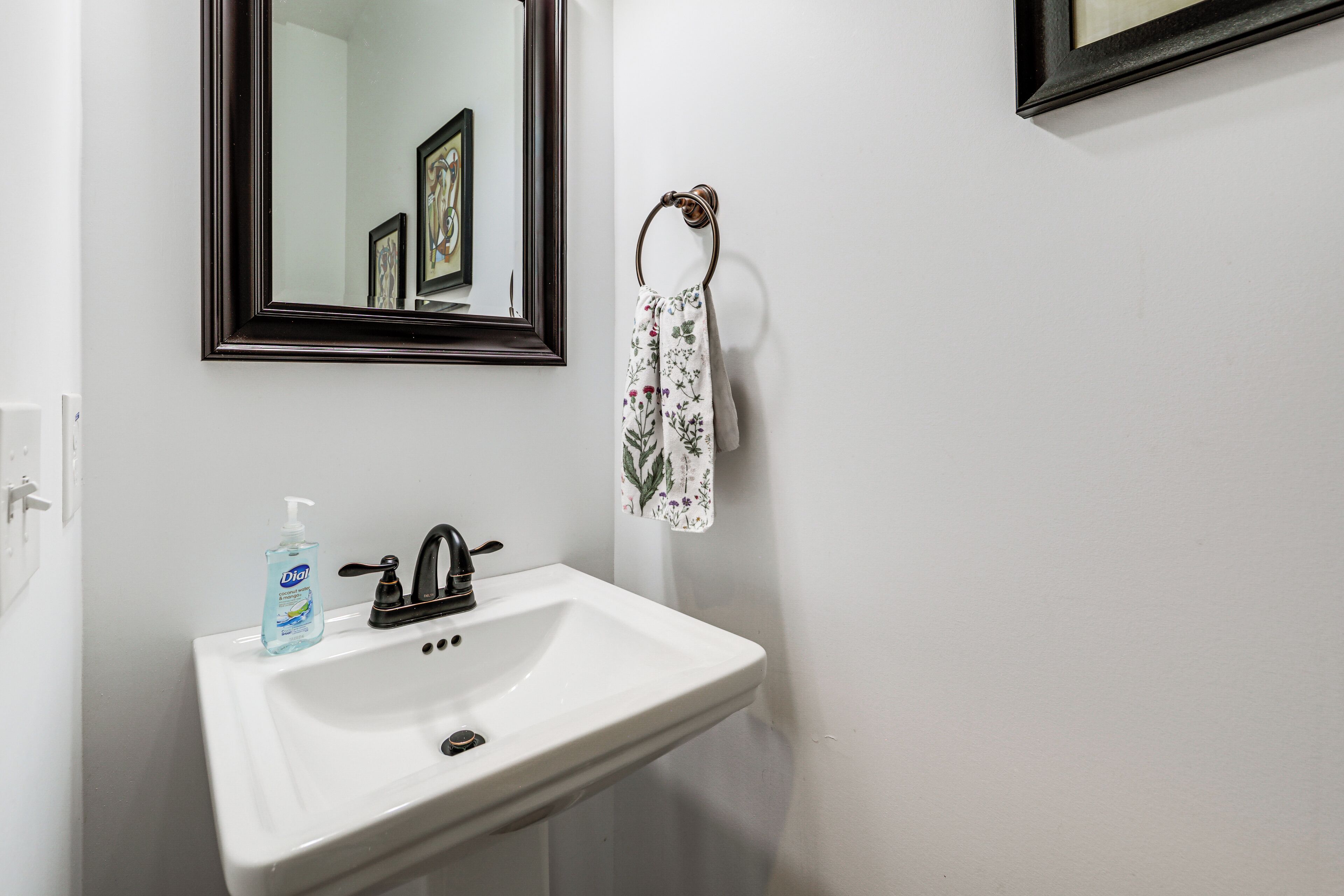 A white bathroom sink with a dark faucet, a mirror above it, and a towel hanging on a metal ring.