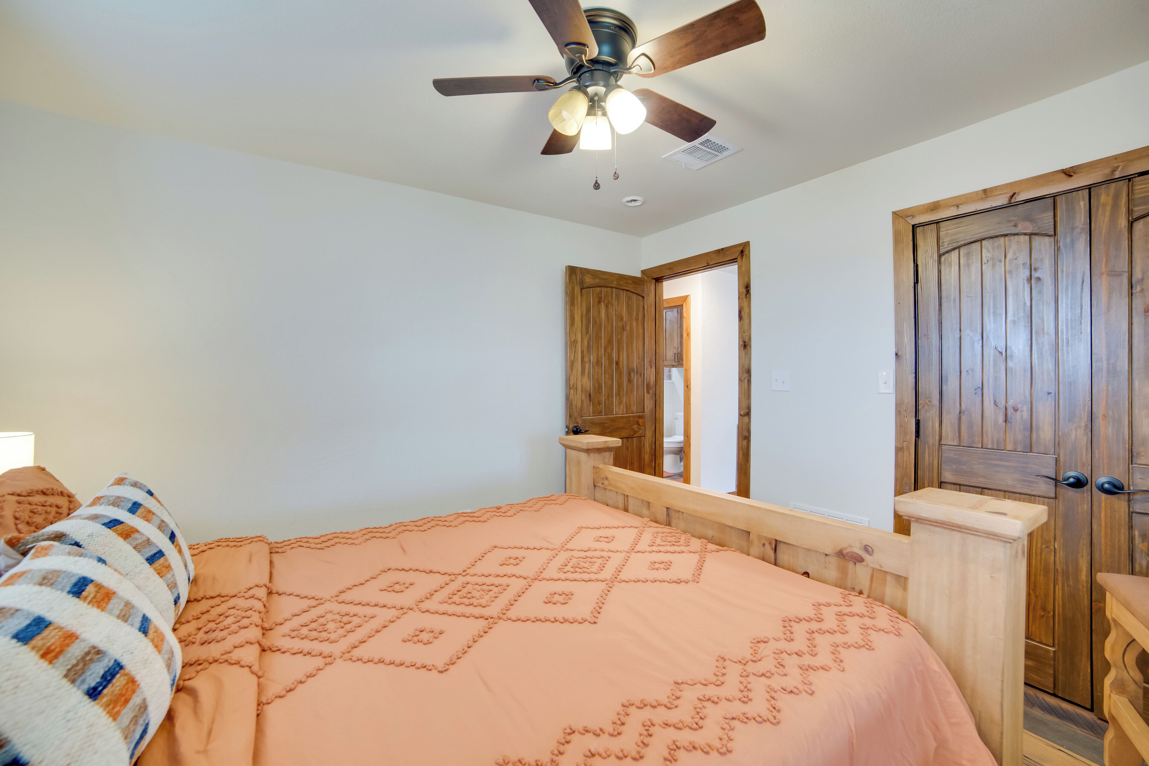 A bedroom with a bed, wooden headboard, ceiling fan, and a door.