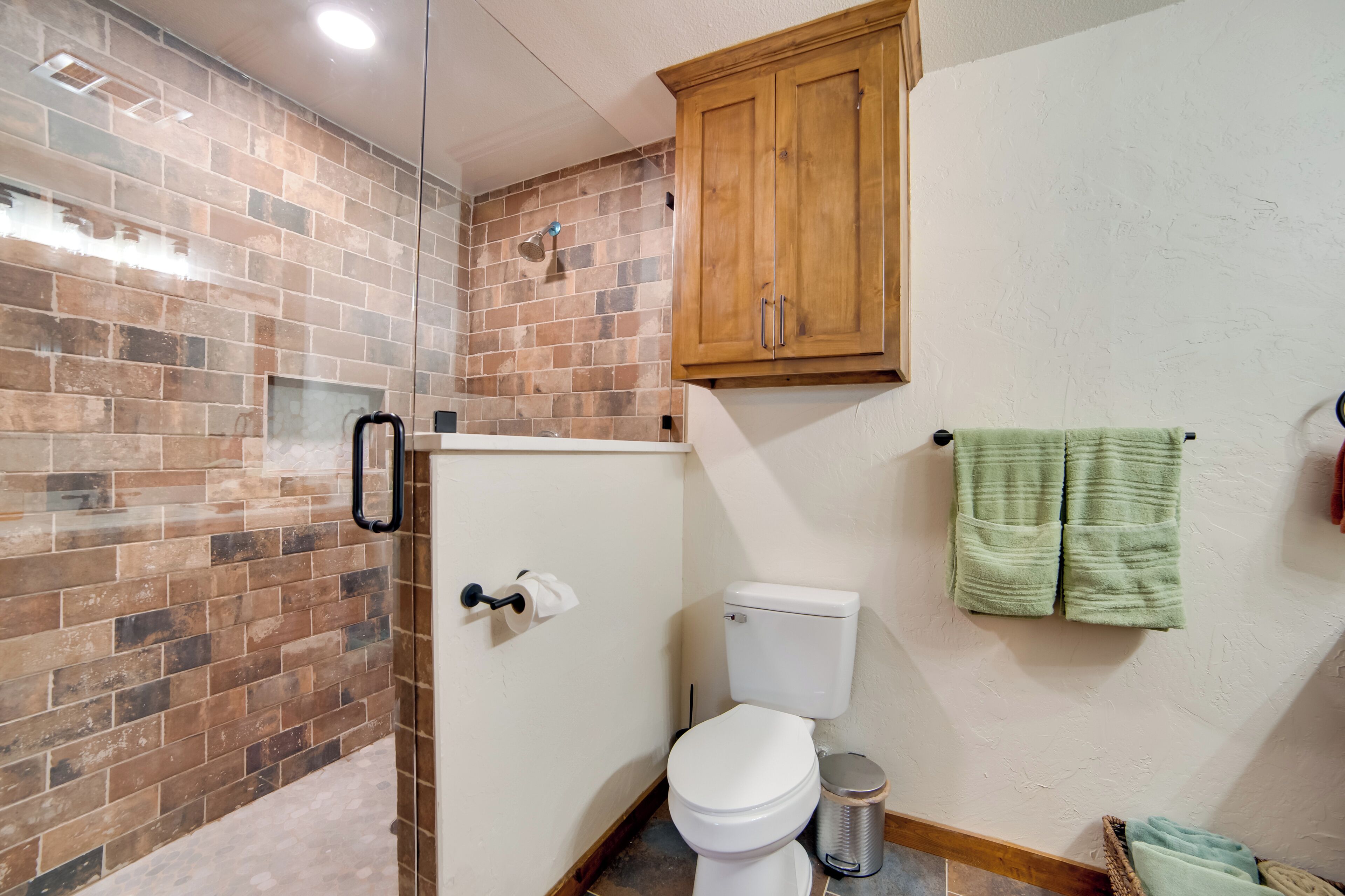A bathroom with a toilet, a shower area, and a wooden cabinet.