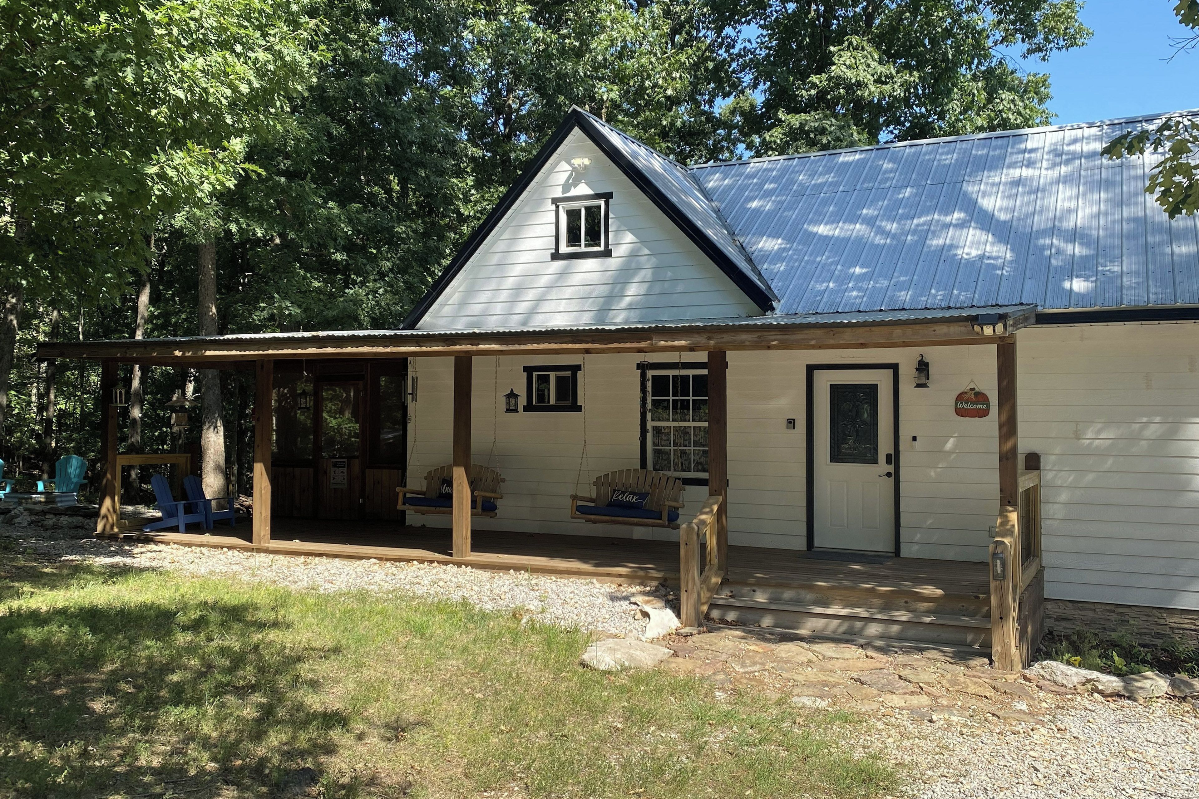 A white building with a metal roof, a porch with wooden chairs, and a welcome sign.
