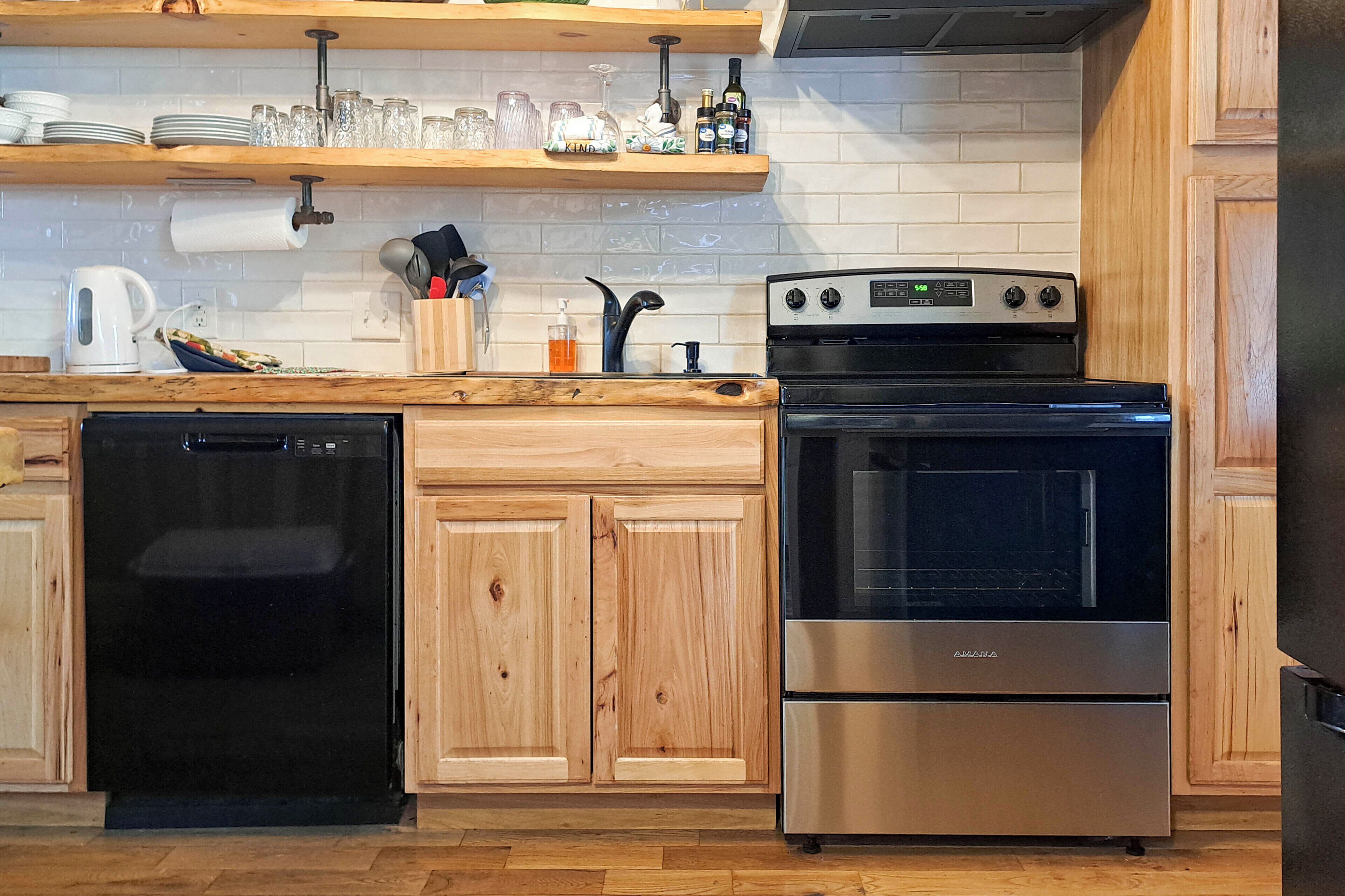 A kitchen with wooden cabinets, a dishwasher, an oven, and a shelf with glassware and bottles.
