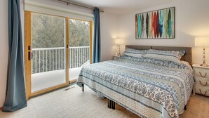 Un dormitorio con una cama grande, una puerta corredera de cristal hacia un balcón y un cuadro abstracto de colores en la pared.