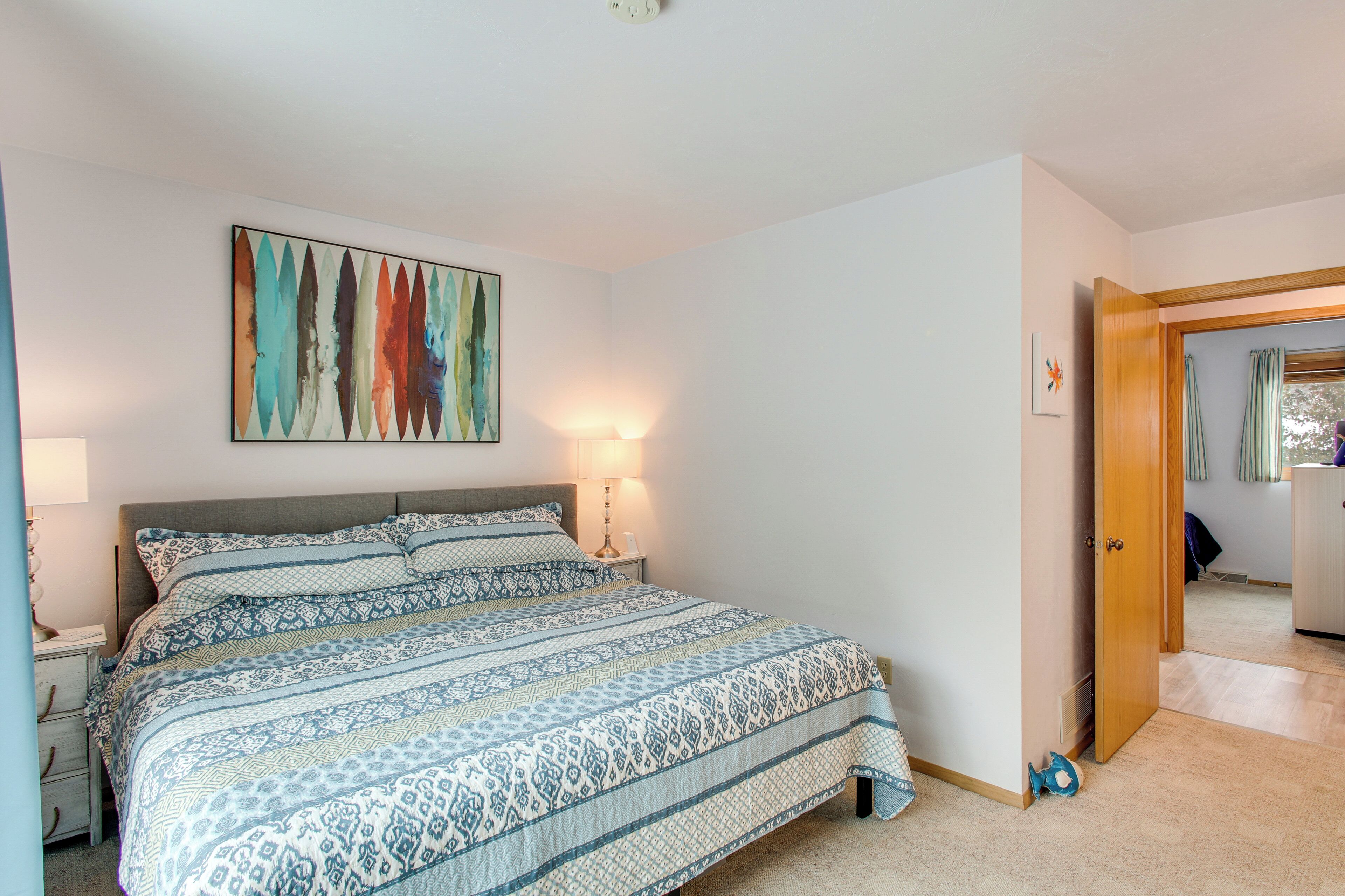 A bedroom with a large bed, a nightstand, a wall-mounted lamp, and a door leading to another room.