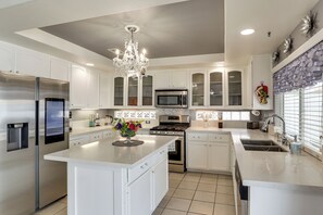 Una cocina moderna con armarios blancos, electrodomésticos de acero inoxidable, una isla central y una araña.
