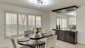 A dining area with a round table, chairs, a vase of flowers, and a dark wooden cabinet with drawers. - Private Pool, Fire Pit & Grills: Las Vegas Getaway (Las Vegas)