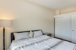 Un dormitorio con cama, mesita de noche, lámpara y una puerta blanca.