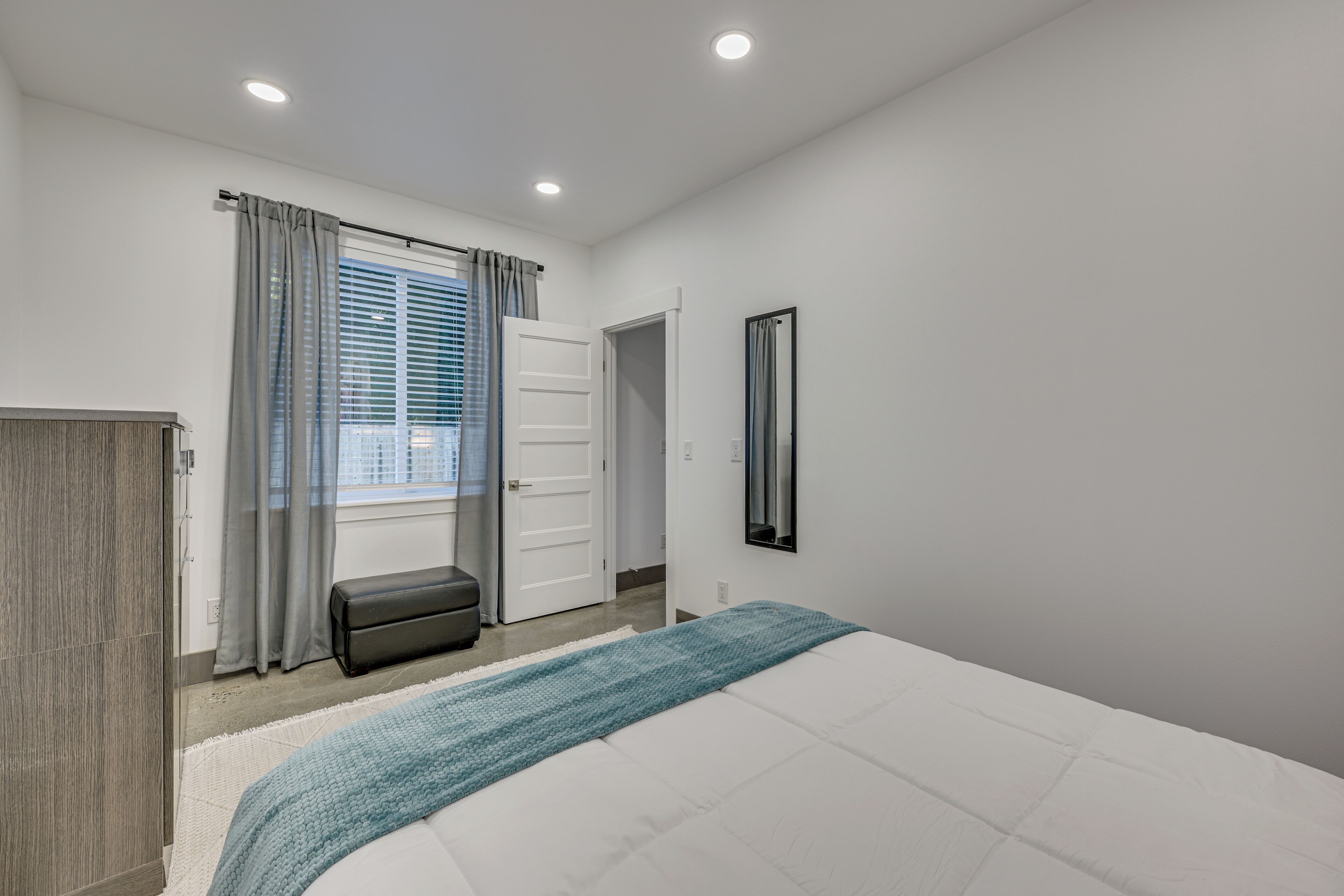 A bedroom with a bed, a bench, a wardrobe, a door, and a window with curtains.