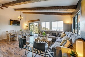 A spacious living room with a large sofa, dining table, and chairs. There is a fireplace, a chandelier, and large windows offering a view of the outdoors. - Modern Heavenly Ski Resort Mountain-top Retreat (Stateline)