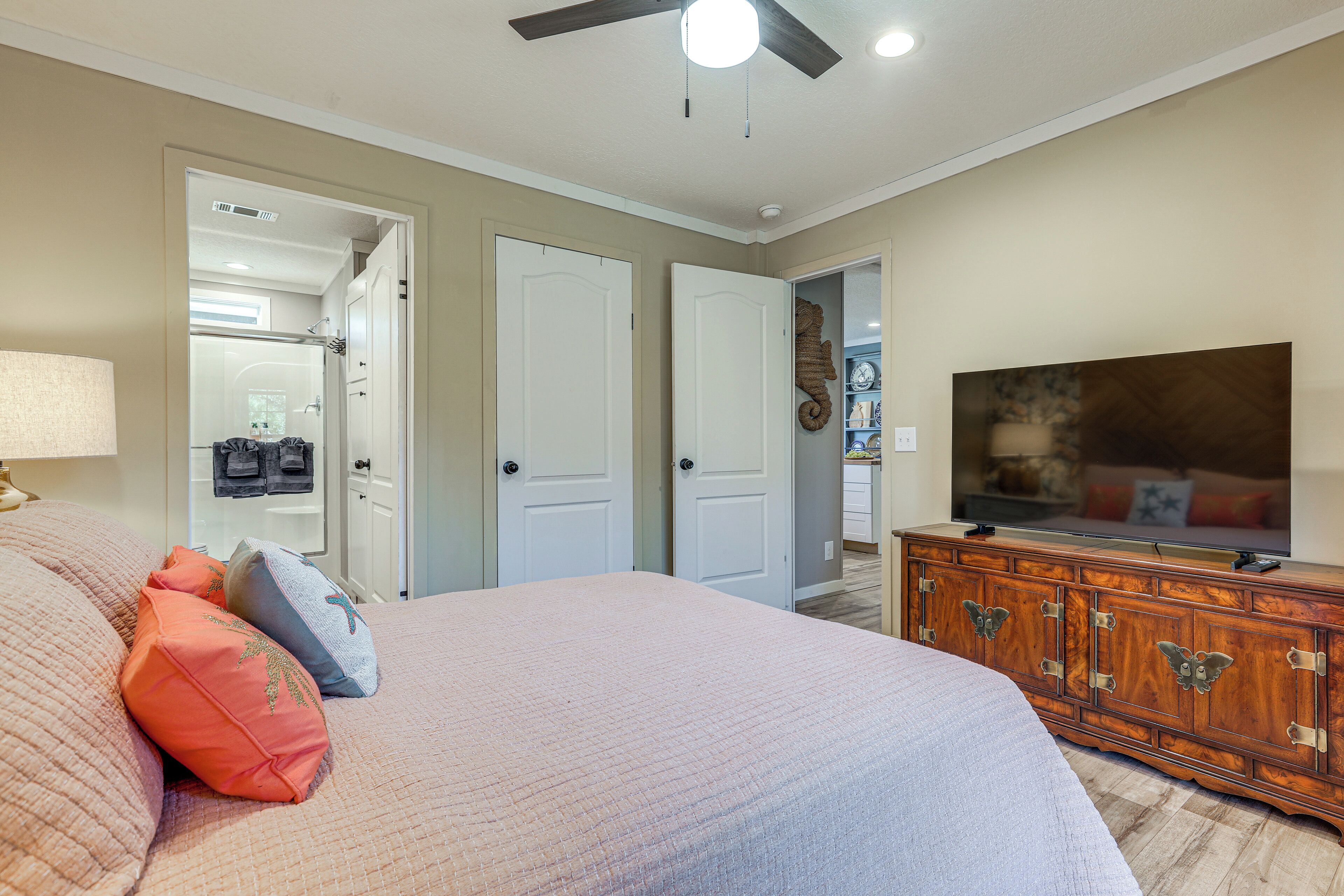 A bedroom with a large bed, a dresser, a television, and a ceiling fan.