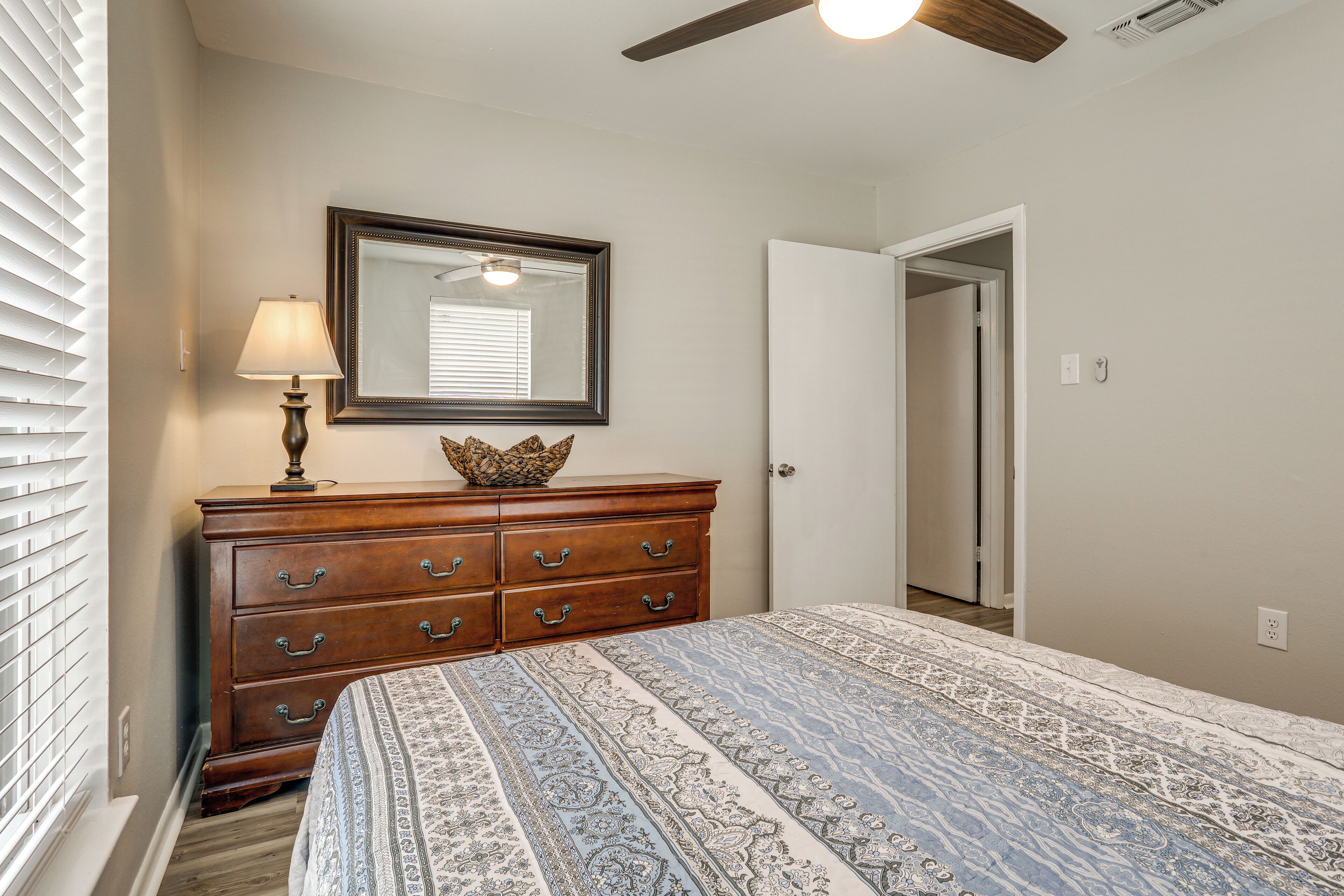A bedroom with a large bed, a wooden dresser with drawers, a mirror above the dresser, and a ceiling fan.