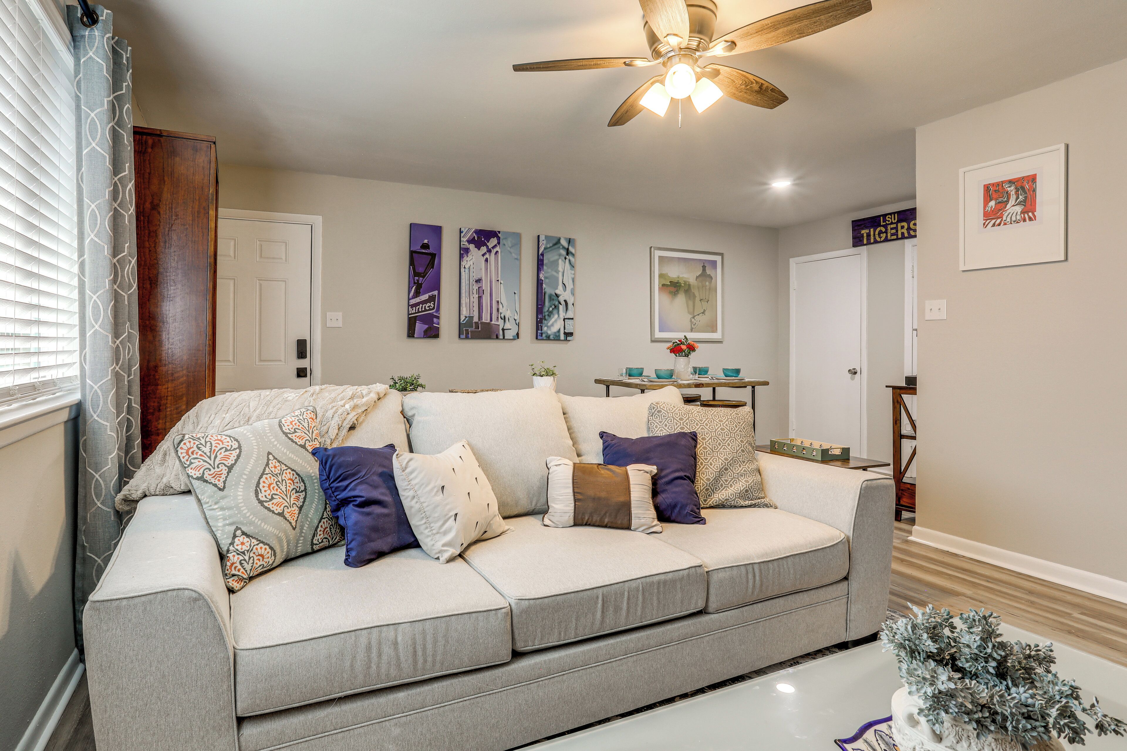 A living room with a grey sofa, decorative pillows, a ceiling fan, wall art, and a door with a sign.