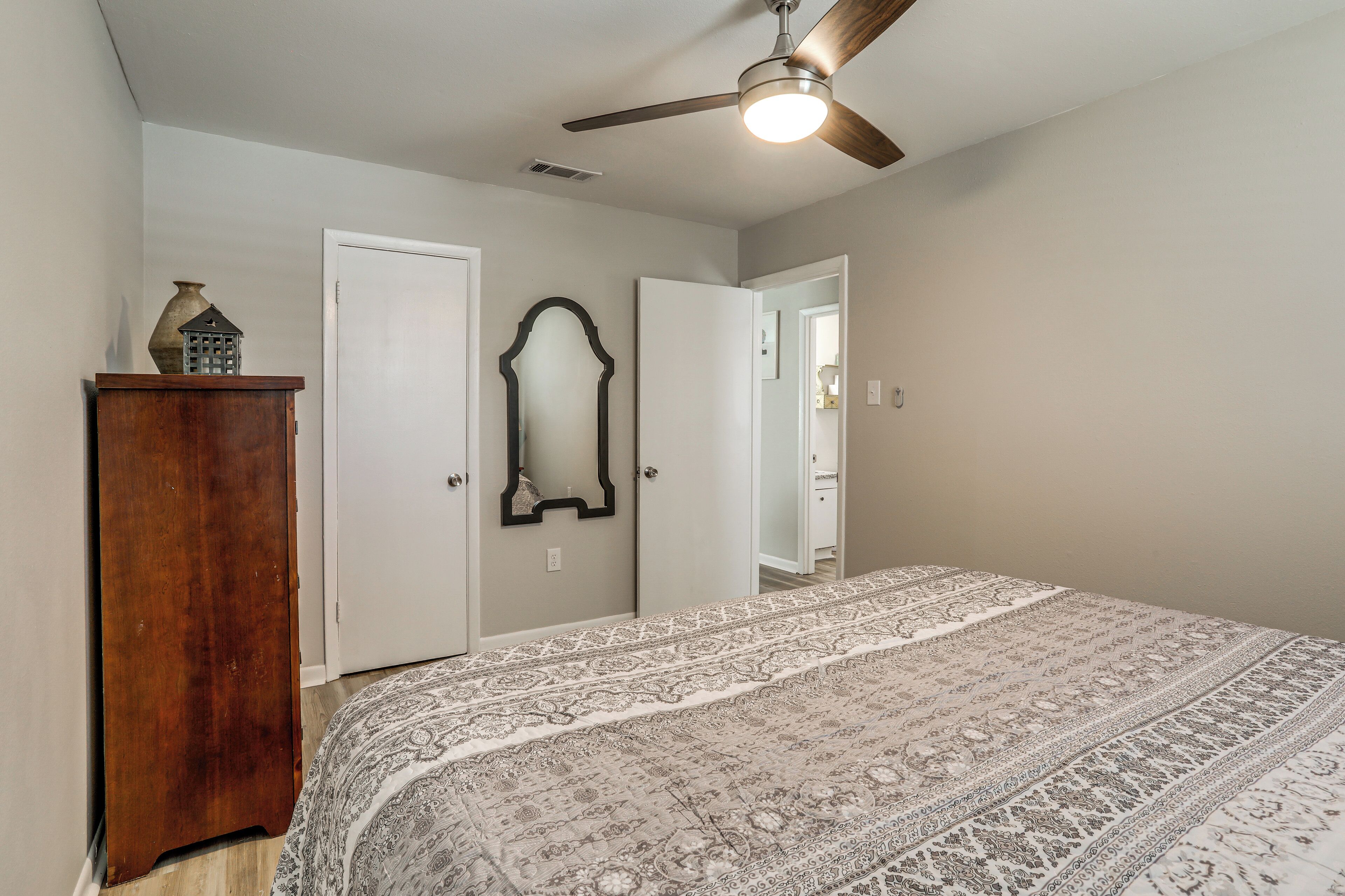 A bedroom with a bed, a ceiling fan, a dresser, and a mirror.