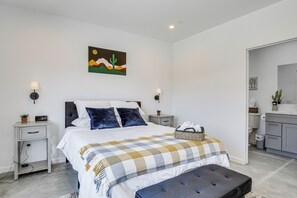 A modern bedroom with a bed, bedside tables, a nightstand, a bench, a wall-mounted artwork, and a bathroom visible through an open door. - 9 Mi to Joshua Tree! Desert Retreat w/ Fire Pit (Yucca Valley)