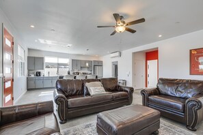 A spacious living area with leather sofas and a ceiling fan, a kitchen in the background, and a red accent wall. - 9 Mi to Joshua Tree! Desert Retreat w/ Fire Pit (Yucca Valley)