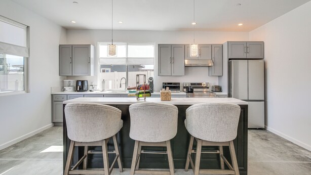 Una cocina moderna con una isla grande, taburetes de bar e iluminación colgante.