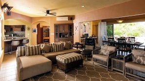 A spacious living area with a large sectional sofa, a dining table with chairs, a kitchen area with a bar, and a ceiling fan. - Steps to Sand: Ocean-view Cabo Home w/ Heated Pool (Cabo San Lucas)