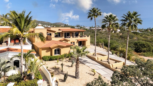 A large, multi-story building with a Mediterranean architectural style, featuring terracotta roof tiles and stucco walls. - Steps to Sand: Ocean-view Cabo Home w/ Heated Pool (Cabo San Lucas)