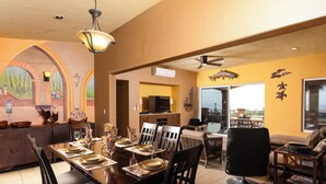 A dining area with a large table set for six, a kitchen in the background, and a view of the outdoors through a glass door. - Steps to Sand: Ocean-view Cabo Home w/ Heated Pool (Cabo San Lucas)