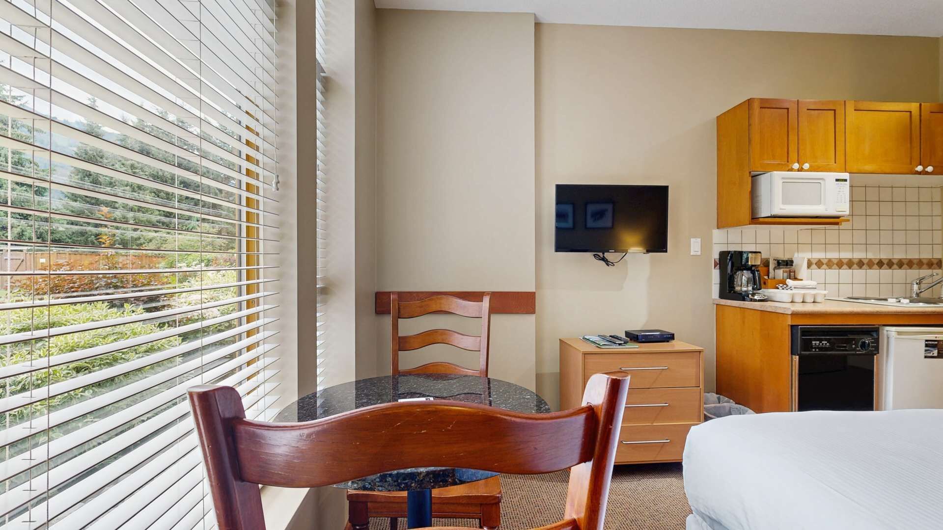 Une chambre d’hôtel équipée d’une table à manger, d’une chaise, d’un lit, d’un téléviseur fixé au mur et d’un coin cuisine avec des placards et un four à micro-ondes.