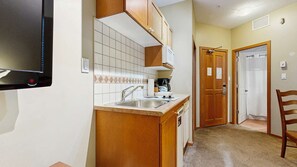 A compact kitchen with a sink, wooden cabinets, and a tiled backsplash.