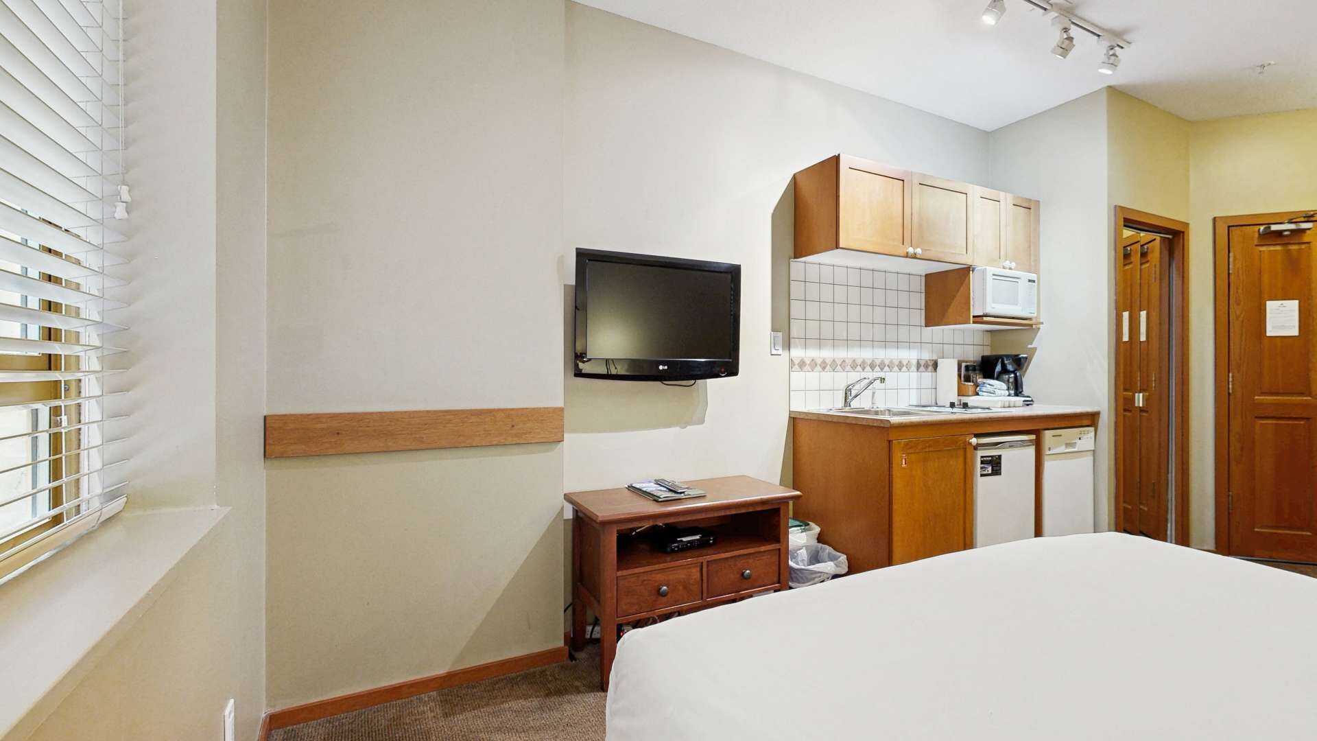 Une chambre d’hôtel équipée d’un lit, d’une télévision, d’une petite armoire en bois, d’un four à micro-ondes et d’un lavabo.