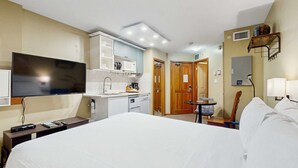 Een hotelkamer met een bed, televisie, kitchenette, een klein tafeltje en een stoel.