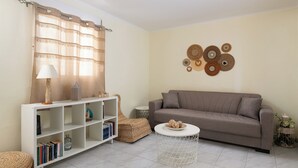 Uma sala de estar com sofá, mesa de centro redonda, estante, objeto decorativo na parede e cadeira de vime.