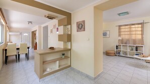 Uma sala de estar espaçosa com uma mesa de jantar e cadeiras, uma estante de livros e uma grinalda decorativa na parede.