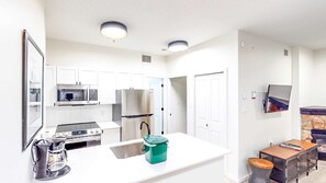 A modern kitchen with white cabinetry, a stainless steel refrigerator, a microwave, and a stove. There is a coffee maker and a green container on the counter.
