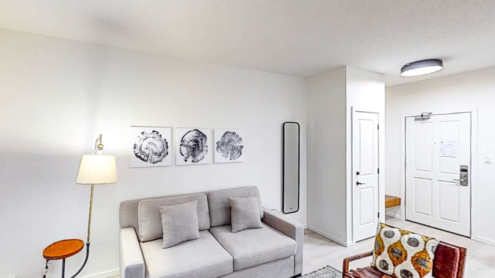 A modern living room with a grey sofa, a floor lamp, and three abstract wall art pieces.