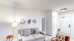 Un salon moderne avec un canapé gris, une lampe sur pied et trois œuvres d’art abstraites accrochées au mur.