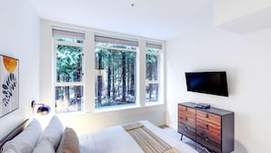 Une chambre avec une grande fenêtre, un lit, une commode et un téléviseur à écran plat.