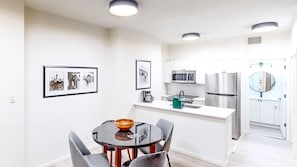 A modern kitchen with white cabinets, stainless steel appliances, and a dining area with a round table and chairs.
