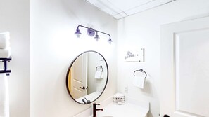 Een badkamer met een grote spiegel, een wastafel, een handdoekhouder en een douche met een handdouche.