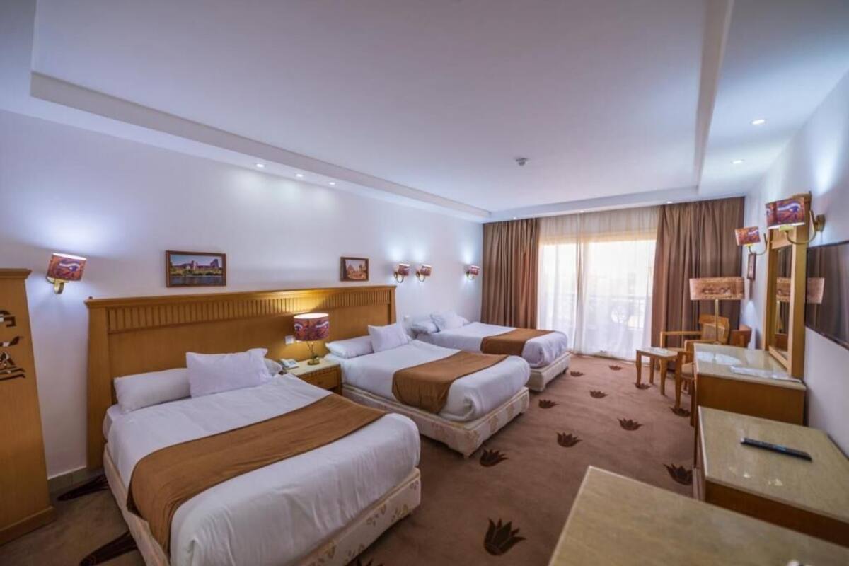 A hotel room with two beds, a desk, a chair, and a television.