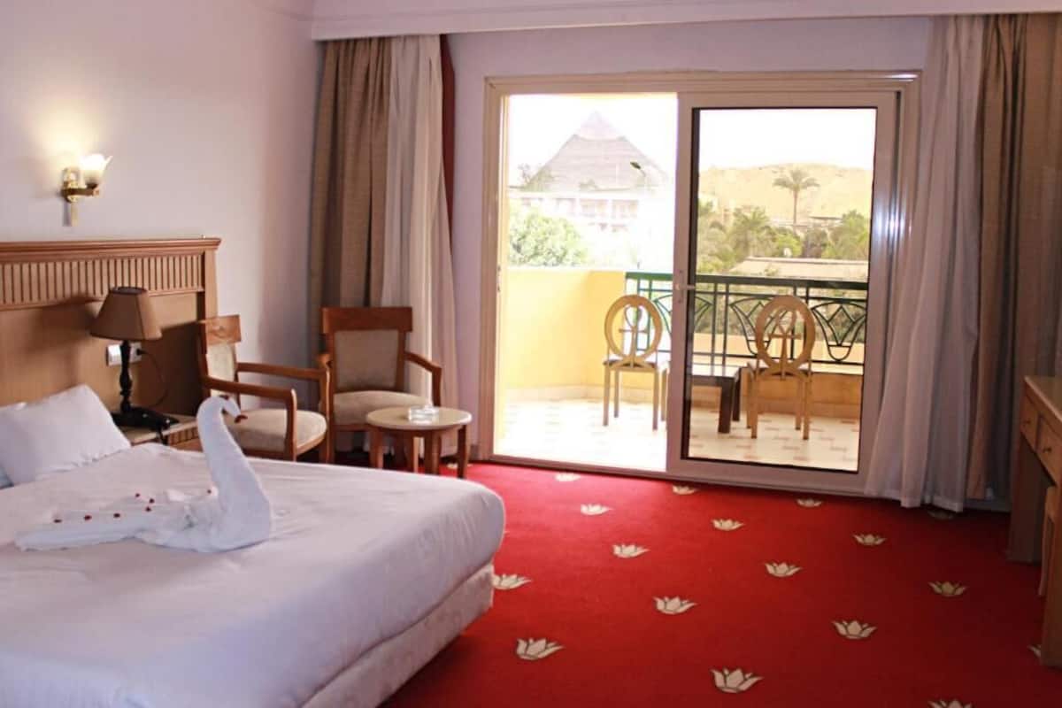 A hotel room with a bed, a chair, a small table, and a balcony with a view of the landscape.