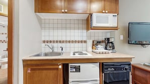 Une cuisine compacte avec des meubles en bois, un four à micro-ondes, une machine à café, un lave-vaisselle et un téléviseur fixé au mur.