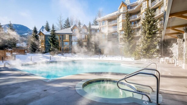 Ein Hotel mit Pool, umgeben von Schnee, mit Wasserdampf und einer Bergkulisse.