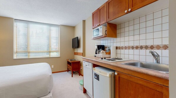 A compact hotel room with a kitchenette, a bed, a TV, and a window with blinds. - Whistler - Cascade Lodge 208 (Whistler)