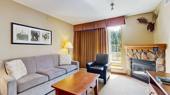 Una sala de estar con sofá, una silla, una mesita de centro, chimenea y una ventana con cortinas.