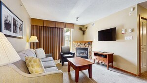 Una sala de estar con sofá, sillón, mesa de centro, chimenea, televisor y una puerta.