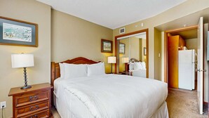 Una habitación de hotel con una cama grande, lámparas de noche, una mesita de noche de madera, un aparador, un refrigerador y un espejo.